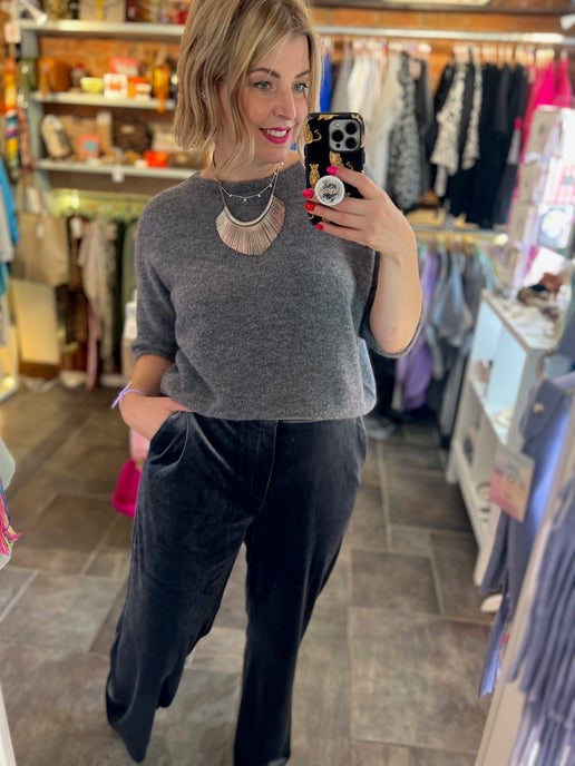 Woman taking a mirror selfie in a clothing store wearing a grey knit alpaca sweater and dark grey velvet trousers