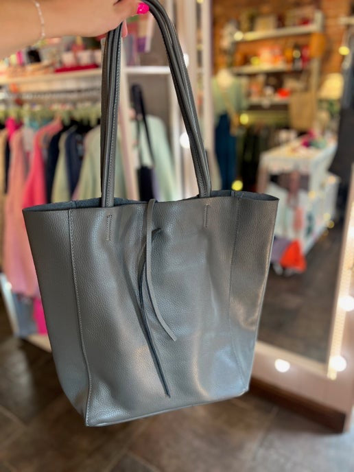 dark grey tote bag held in a store setting with blurred background