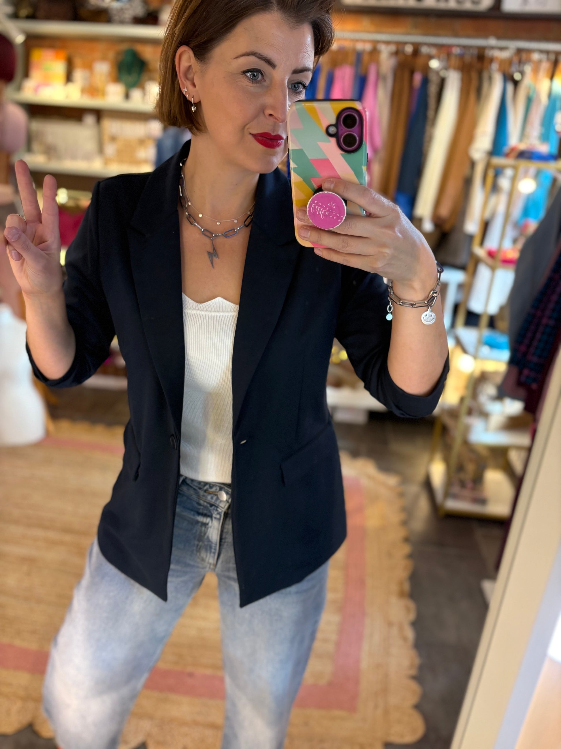 Woman taking a mirror selfie wearing a  tailored dark navy blazer and light blue jeans in a store.