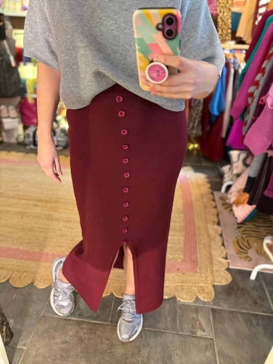 Person wearing a gray shirt and maroon skirt with a colorful phone case, standing in a store.
