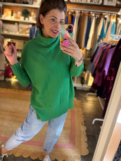 Woman taking a mirror selfie wearing a green ribbed long sweater in a clothing store.