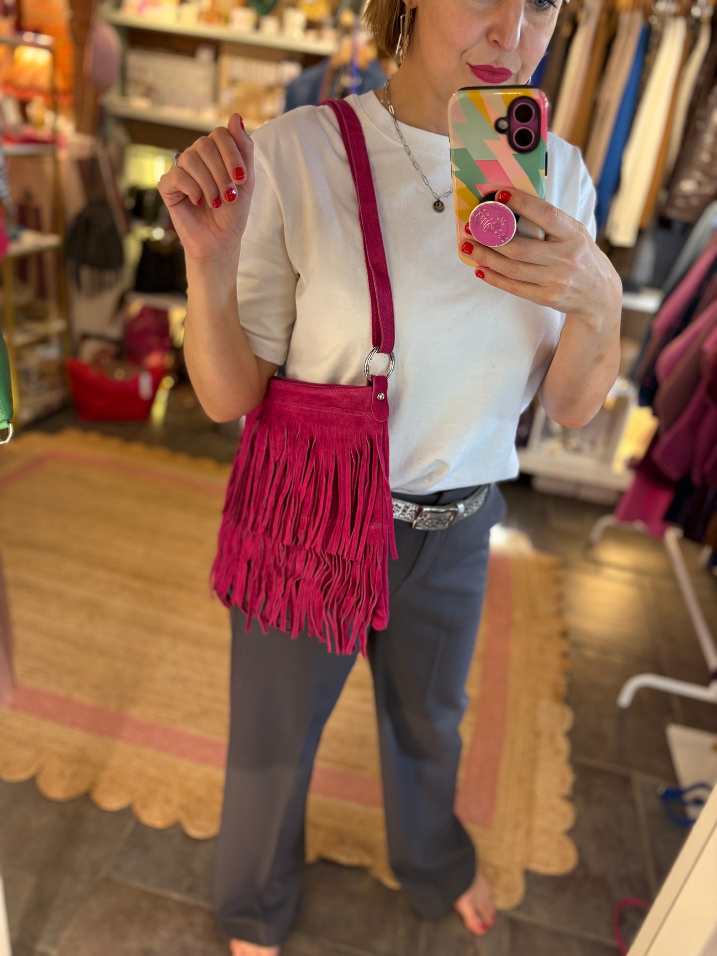 Person taking a mirror selfie wearing a white shirt, dark grey trousers, and a pink fringed bag.