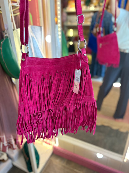 Pink fringed suede handbag with a tag in a store setting