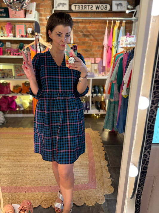 Person taking a mirror selfie wearing a plaid dress in a store.