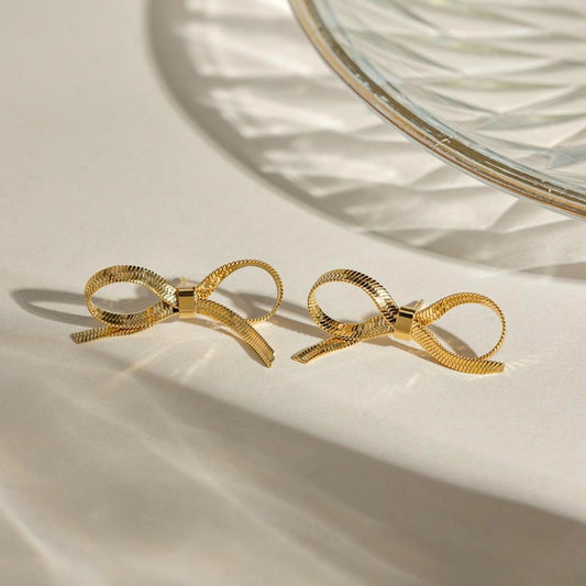 Gold bow-shaped hair clips on a beige surface with a glass bowl in the background