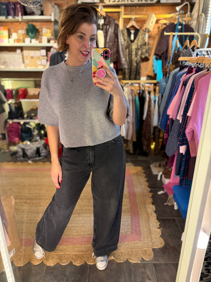 Person taking a mirror selfie wearing a gray sweater and black pants in a clothing store.