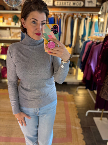 Woman taking a mirror selfie in a clothing store wearing a grey fine knit roll neck jumper and jeans.