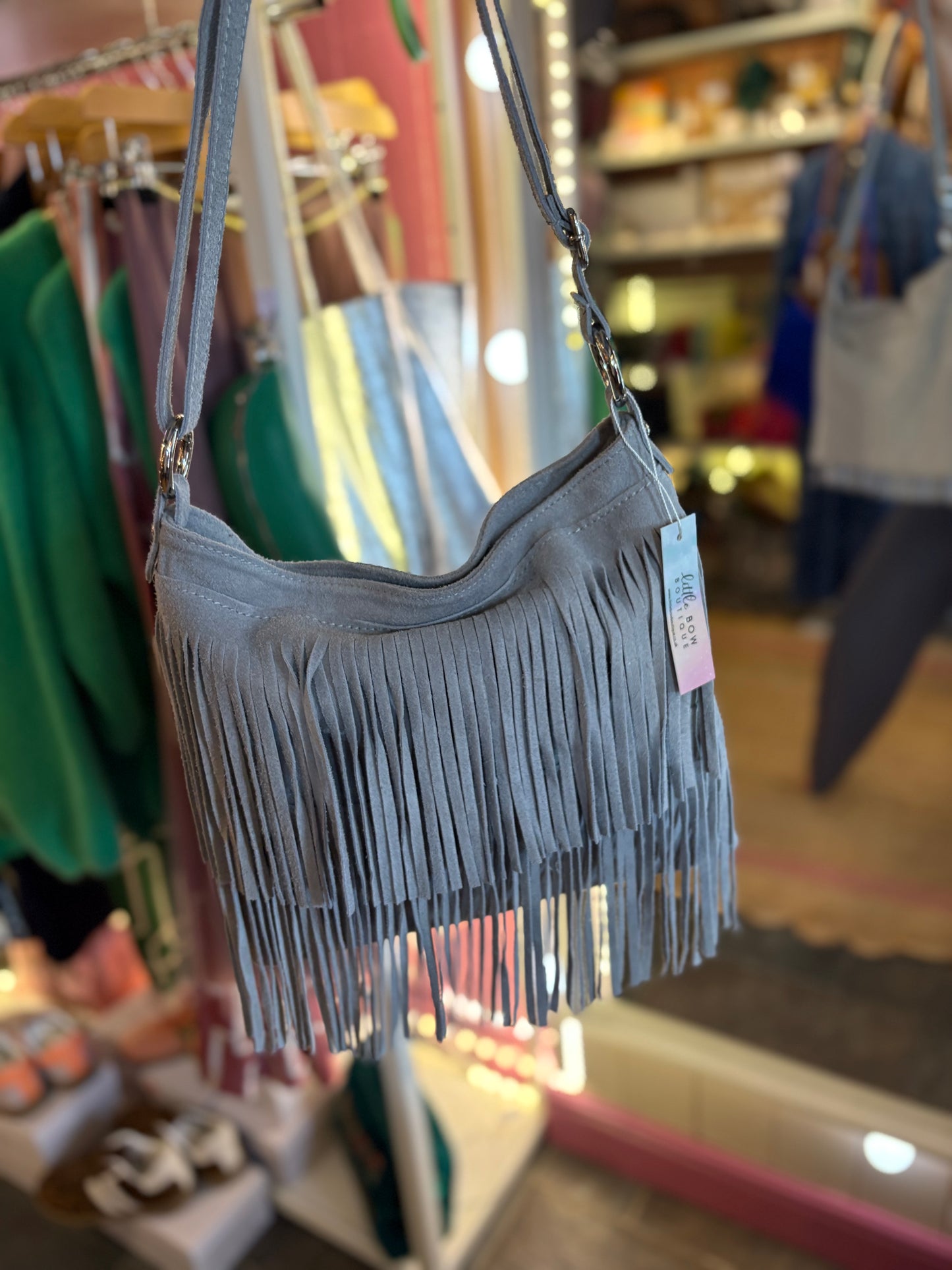 Grey fringe suede handbag with a tag on a rack in a store