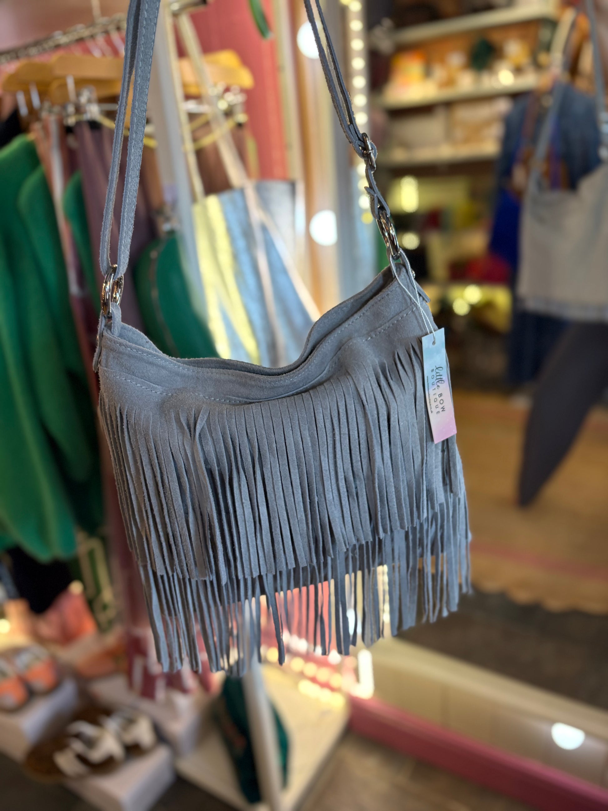 Grey fringe suede handbag with a tag on a rack in a store