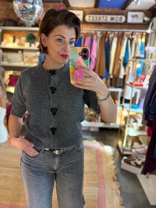 Woman taking a mirror selfie wearing a grey cardigan and jeans in a store.