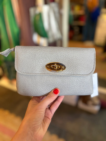 Light gray textured wallet with gold clasp held by a hand against a blurred indoor background