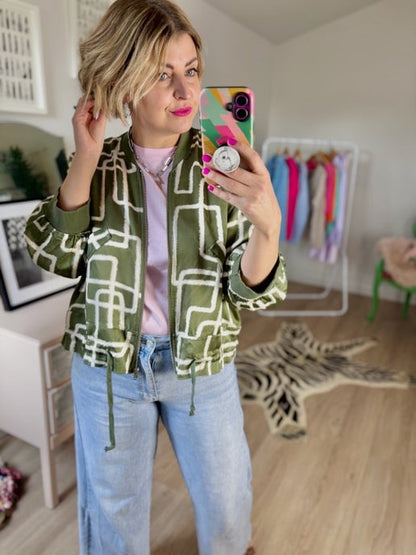 Person taking a mirror selfie wearing a khaki green patterned jacket and light blue jeans 