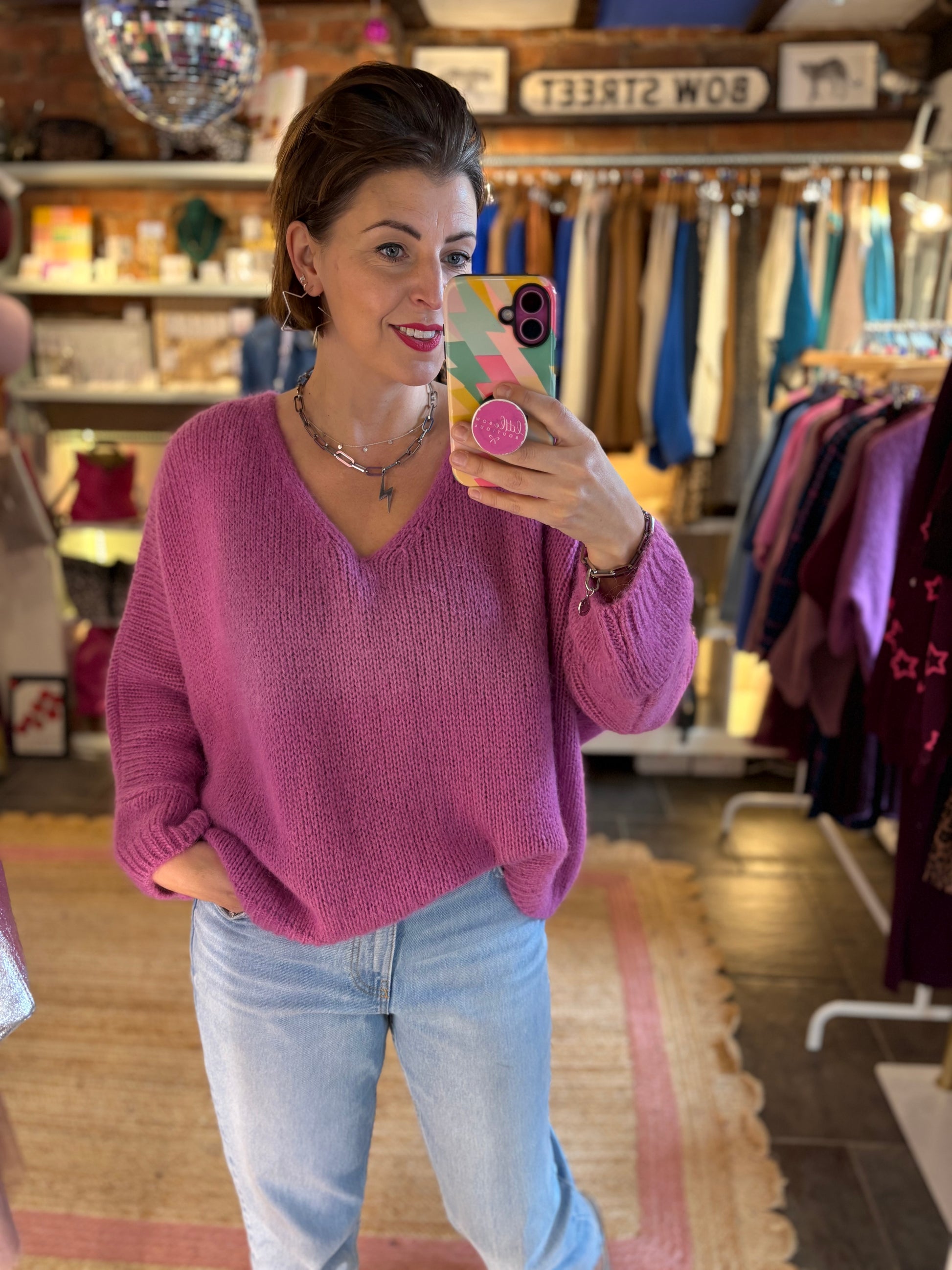 Woman taking a mirror selfie wearing a pink sweater and blue jeans in a store.