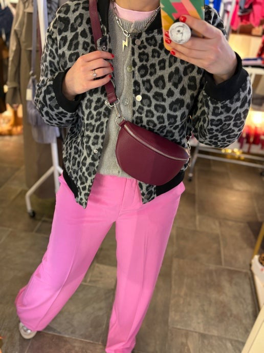 burgundy leather crossbody half moon shape bag worn with leopard print bomber jacket and pink trousers