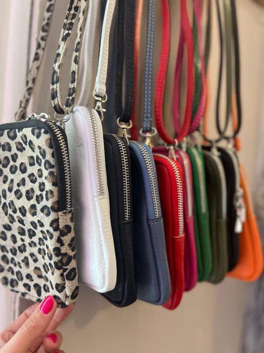 Row of small handbags with different designs and colors hanging on a rack.
