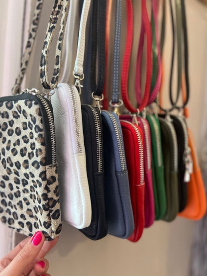 Row of small handbags with different designs and colors hanging on a rack.