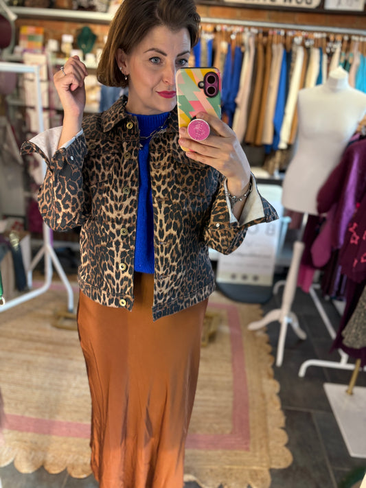 Person taking a mirror selfie wearing a leopard print jacket and brown skirt in a clothing store.