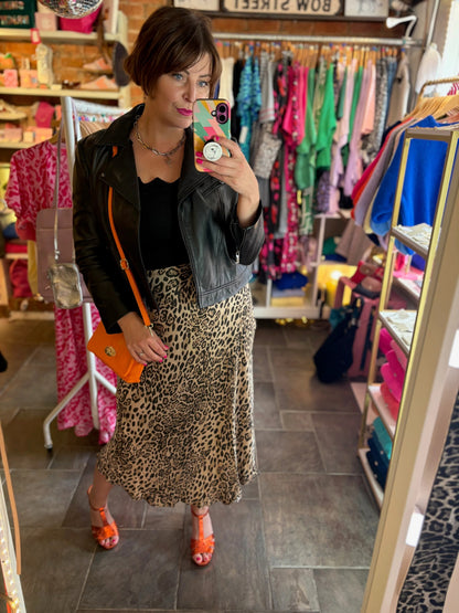 Person taking a mirror selfie in a clothing store wearing a leopard print skirt and black jacket.