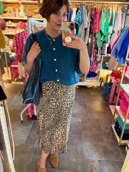 Woman taking a mirror selfie wearing a teal shirt and leopard print skirt in a store.