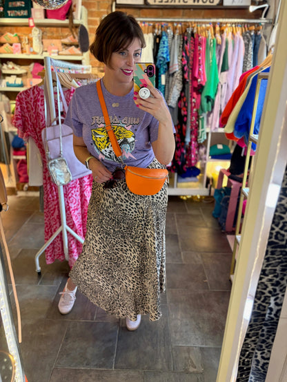 Woman taking a mirror selfie in a clothing store wearing a graphic t-shirt and leopard print skirt.