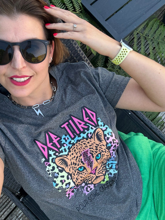 Person wearing a gray t-shirt with a colorful leopard graphic design, sitting outdoors.