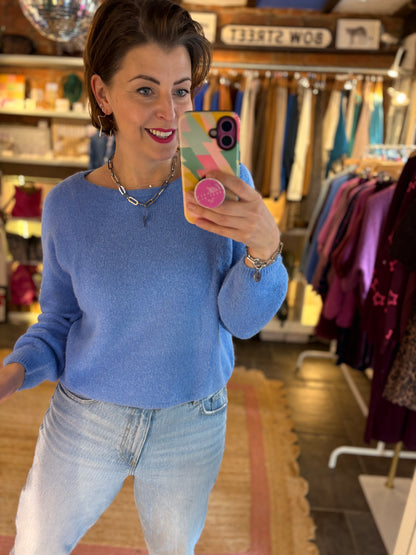 Woman taking a mirror selfie wearing a blue knit jumper and jeans in a clothing store.