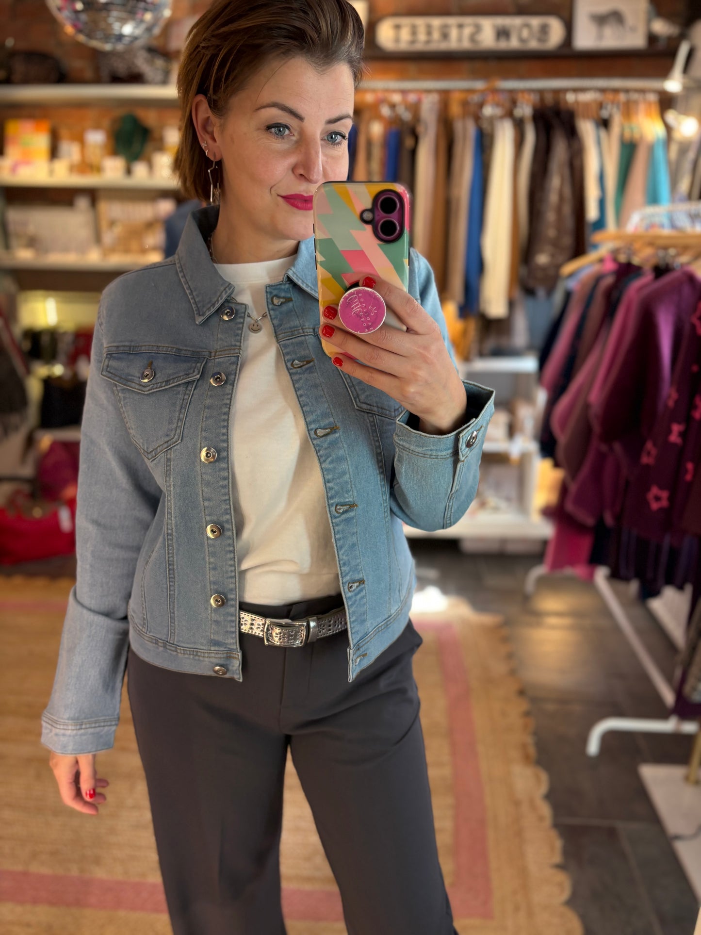 Woman taking a mirror selfie wearing a denim jacket in a clothing store.