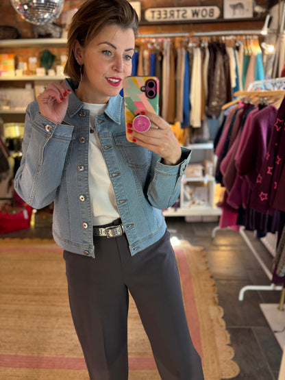 Woman taking a mirror selfie in a clothing store wearing a denim jacket and grey trousers