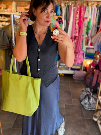 Woman taking a mirror selfie in a clothing store holding a green tote bag.