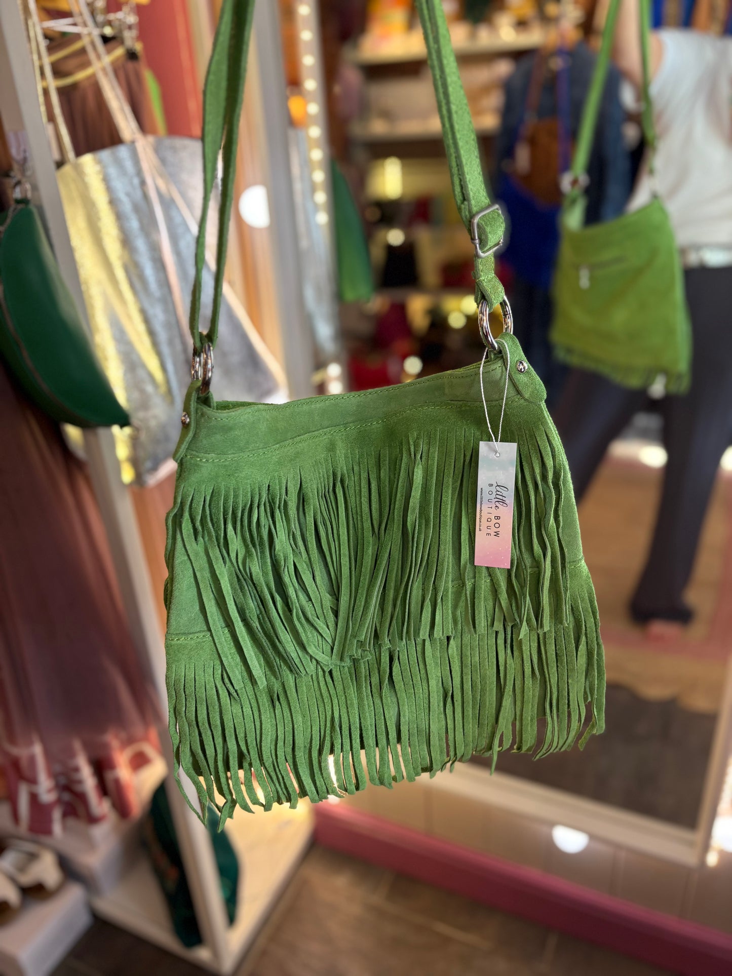 Green fringed suede handbag with a tag on a rack in a store setting