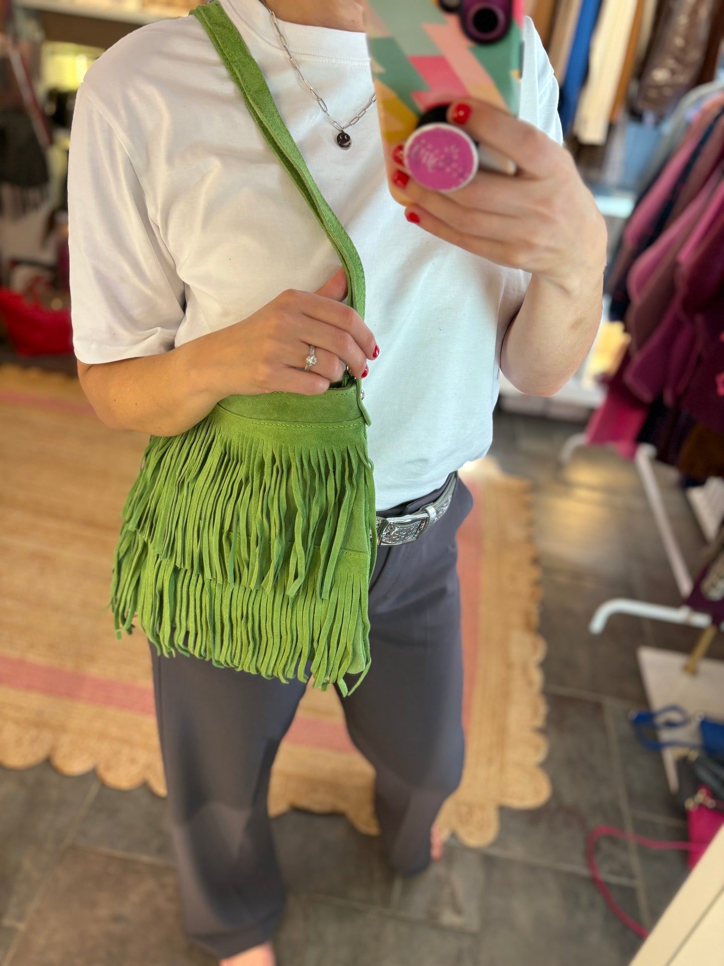 Person holding a lime green fringed suede bag in a store setting