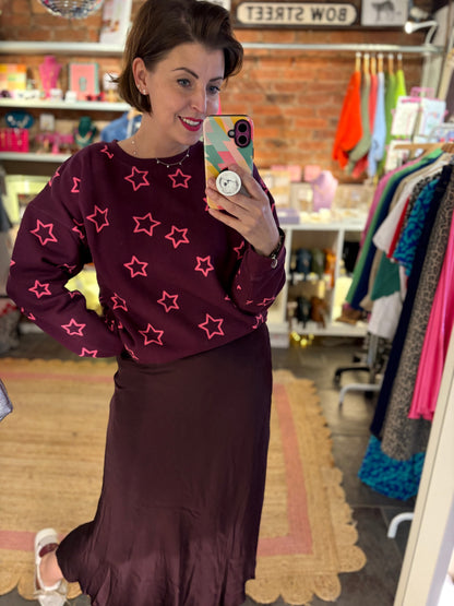 Woman taking a mirror selfie wearing a maroon sweater with pink star patterns and a matching skirt in a store.