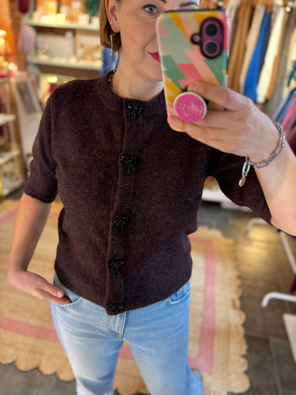 Person taking a mirror selfie wearing a merlot burgundy cardigan and light blue jeans in a store setting.