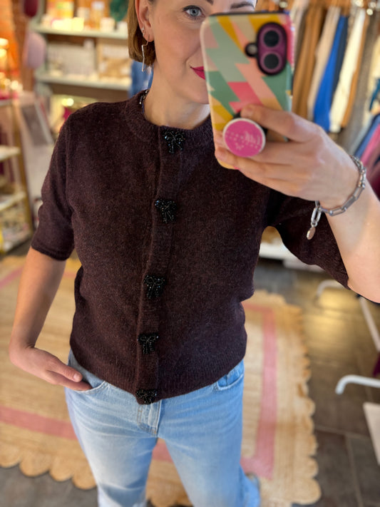 Person taking a mirror selfie wearing a merlot burgundy cardigan and light blue jeans in a store setting.