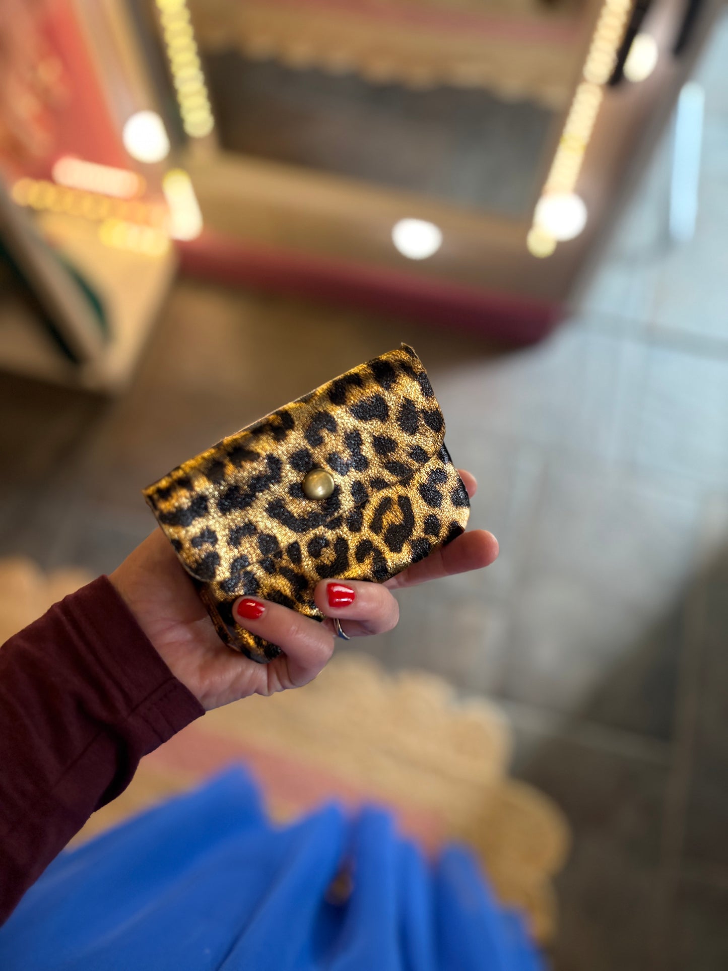 Hand holding a leopard print leather purse for coins and cards.
