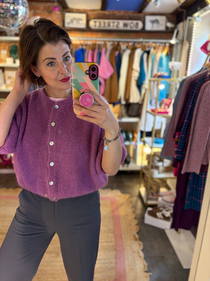 Woman taking a mirror selfie wearing a purple cardigan in a clothing store.