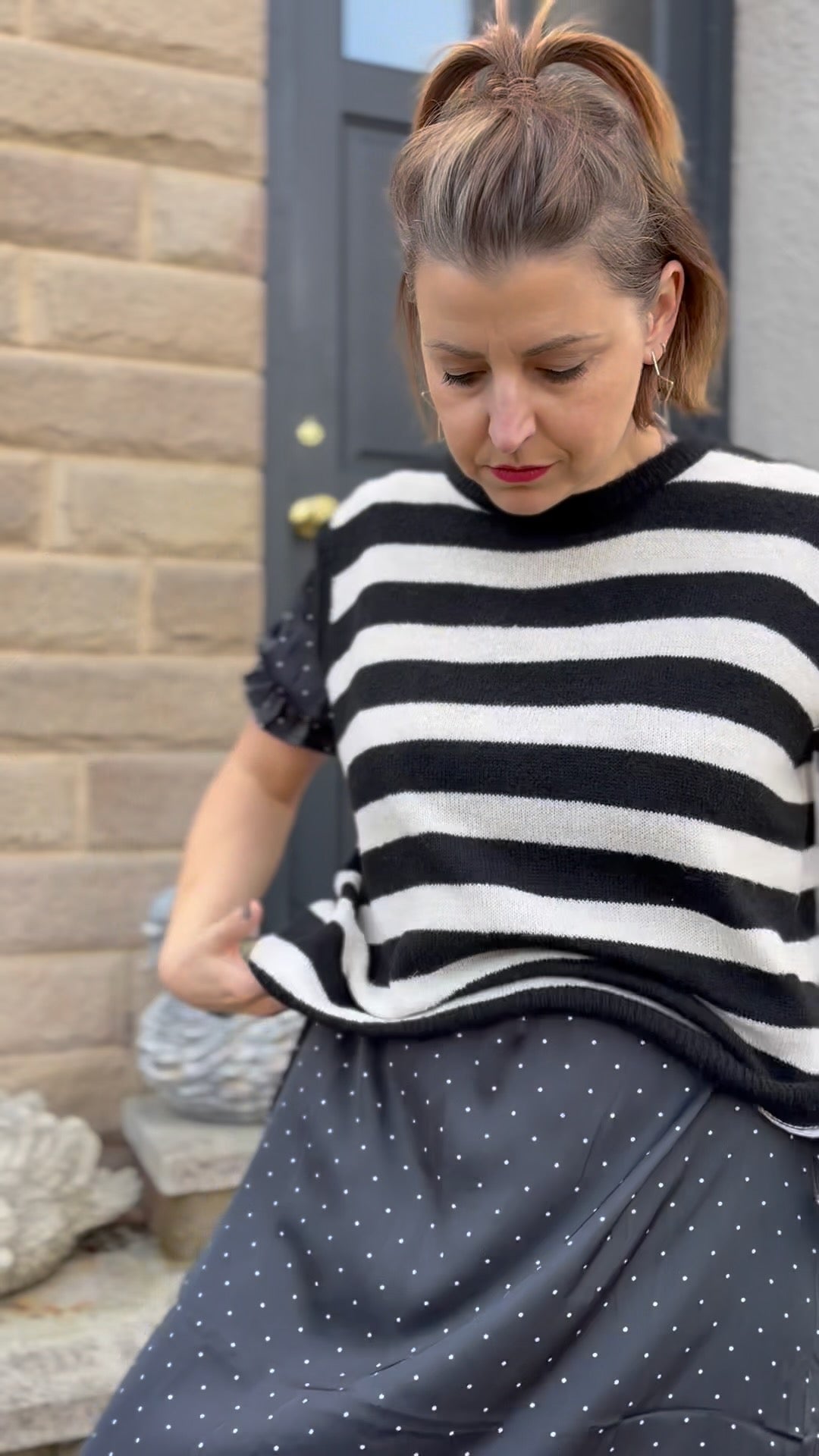 Woman wearing a black and white striped sweater and dark polka dot skirt outdoors.