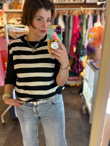 Woman taking a mirror selfie wearing a black and white striped sweater layered over a black top and jeans in a store.