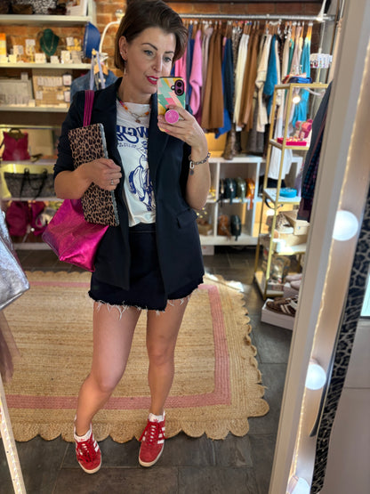 An outfit of a woman dressed in a dark navy blue blazer, indigo blue denim skirt, white graphic print t-shirt and pink metallic tote bag.