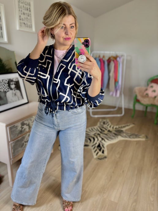 Woman taking a mirror selfie wearing a navy patterned jacket and light blue jeans 