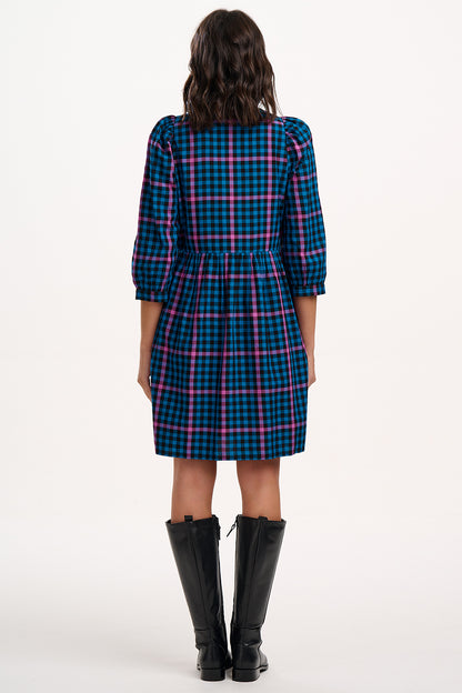 Person wearing a blue and pink plaid dress with black knee-high boots on a white background
