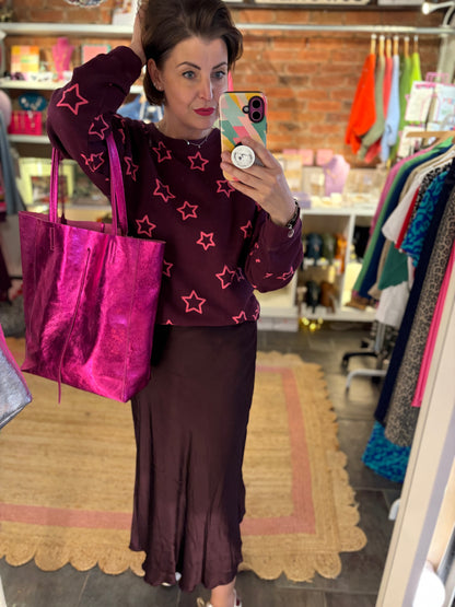 Woman taking a mirror selfie in a clothing store holding a pink bag.