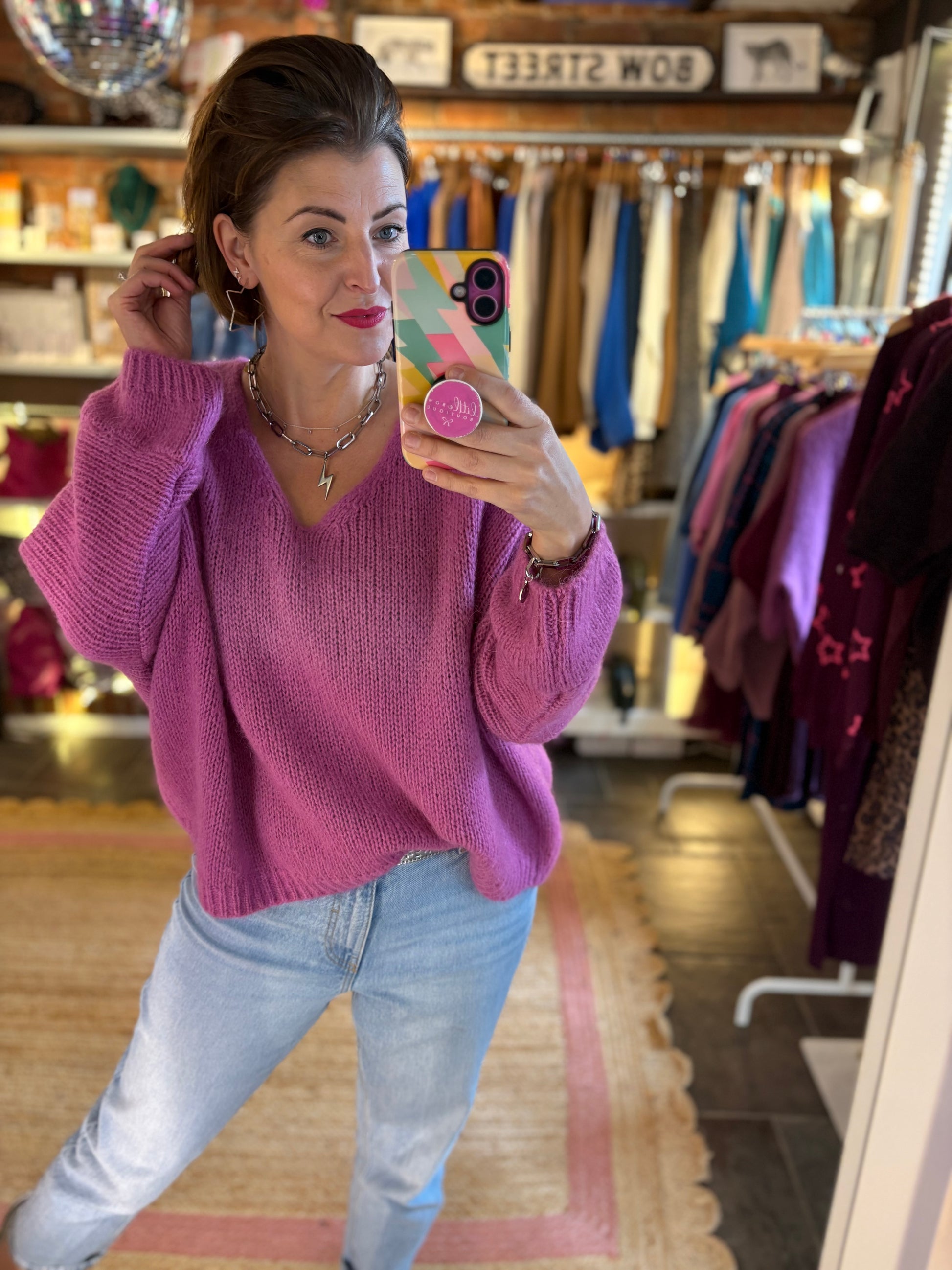 Woman taking a mirror selfie wearing a pink slouchy knitted mohair jumper and light blue jeans in a clothing store.