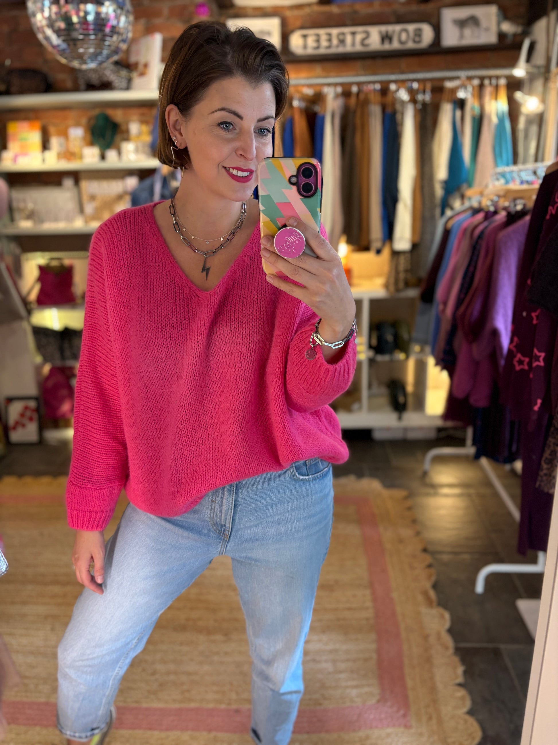 Woman taking a mirror selfie wearing a pink mohair sweater and blue jeans in a clothing store.