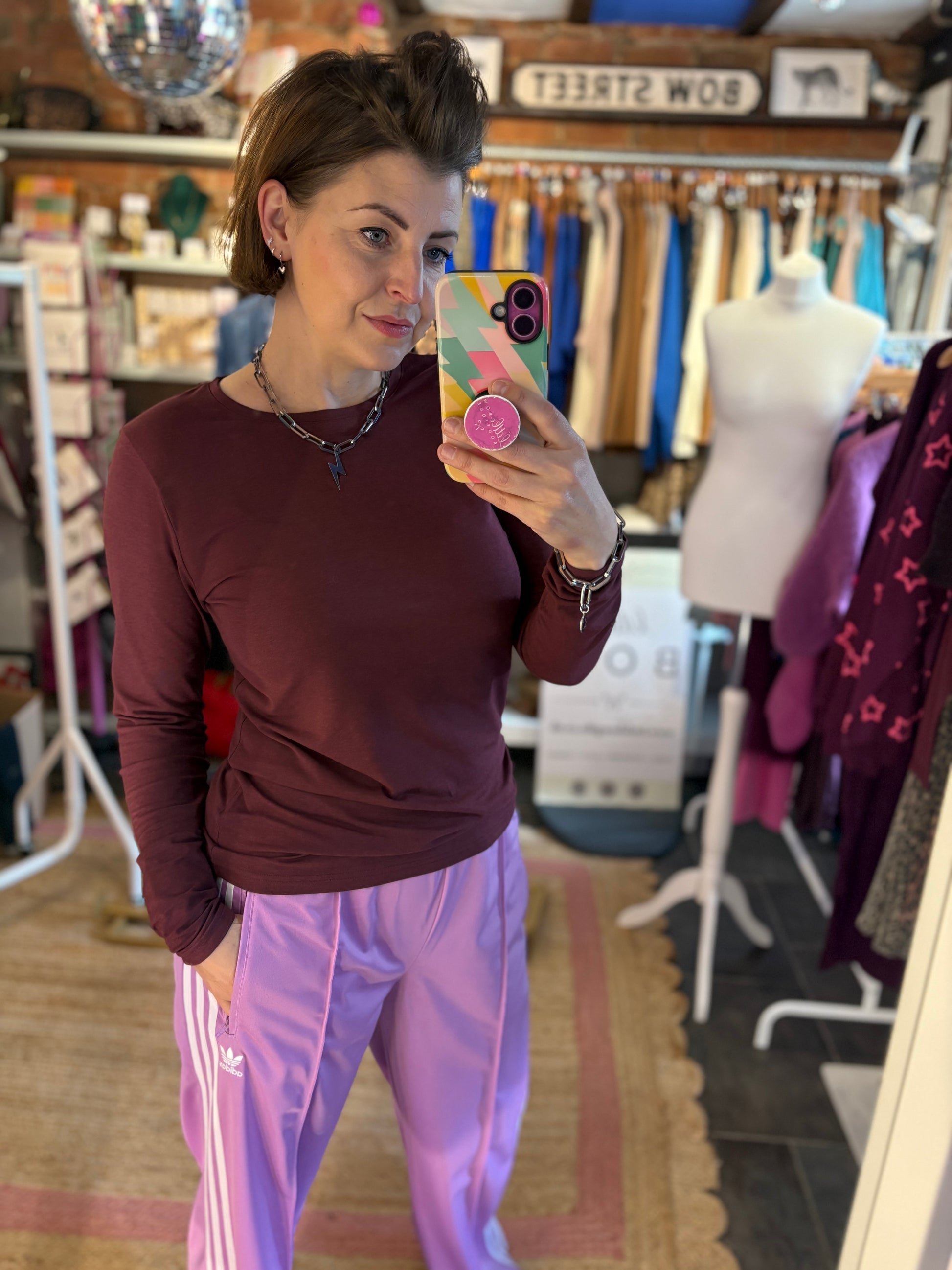 Woman taking a mirror selfie wearing a maroon long-sleeve top and pink pants in a clothing store.