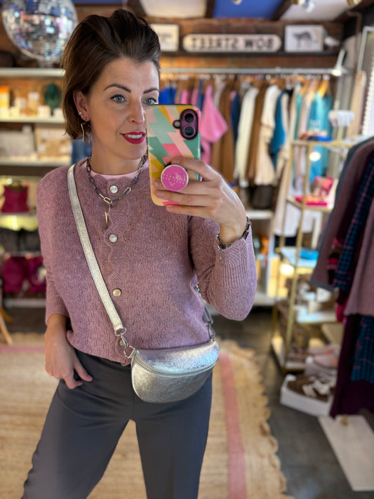 Woman taking a mirror selfie in a store wearing a mauve pink cardigan and grey pants.