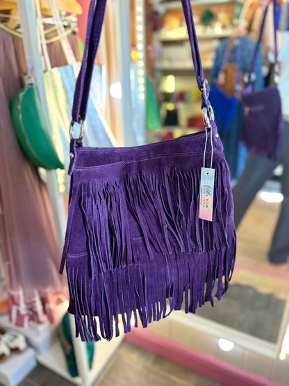 Purple fringe suede handbag with a crossbody adjustable strap in a store setting