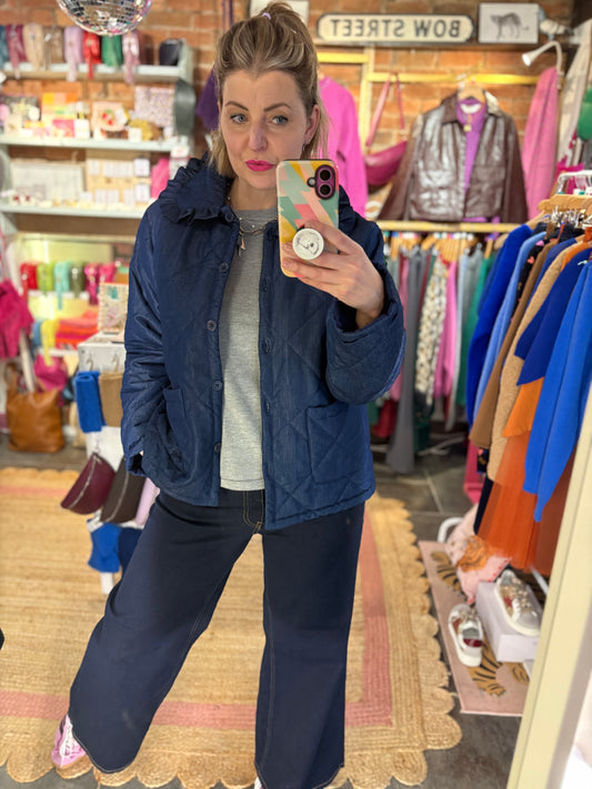 Woman taking a mirror selfie wearing a navy blue jacket and pants in a store.