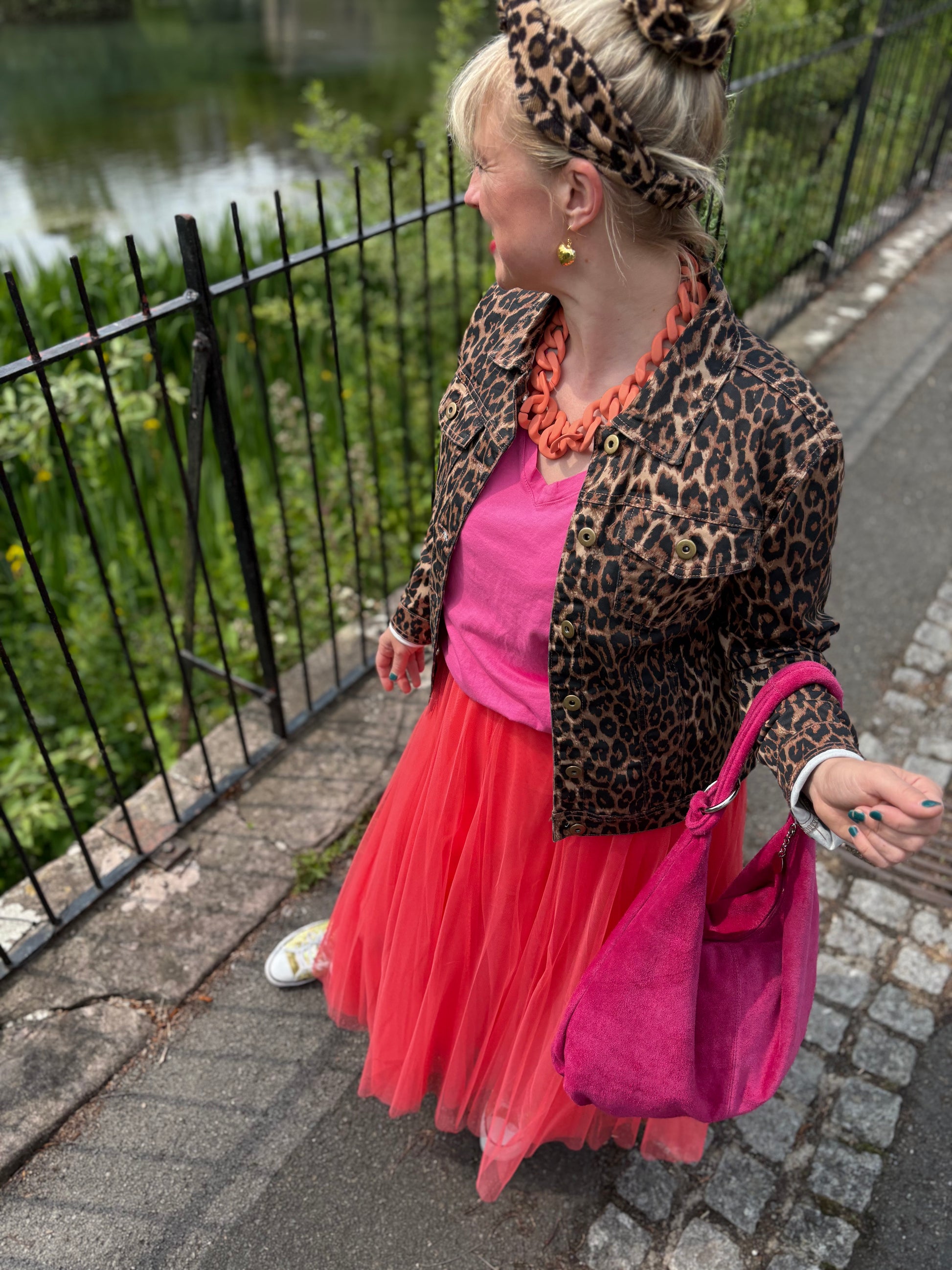 Person wearing a leopard print jacket and pink dress with a pink bag, standing on a sidewalk.