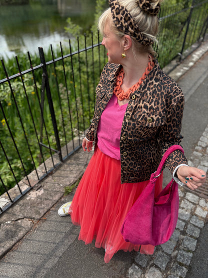 Person wearing a leopard print jacket and pink dress with a pink bag, standing on a sidewalk.